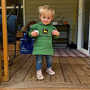Aurora is registered to the contest to win money with this photo: toddler, child, hoodie, green_clothing, jeans, socks, shoes, porch, wooden_floor, smile, blonde_hair, holding_objects, balls, home, chair, water_jugs, rug, doorway, outdoor, person