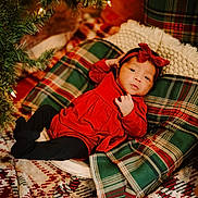 Eliana joined the competition — help win amazing prizes! baby, infant, red_dress, headband, plaid, pillow, blanket, christmas_tree, holiday, decorations, lights, cozy, indoor, pattern, soft_fabric, child, cute, festive, portrait, relaxing