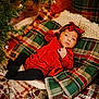 baby, infant, red_dress, headband, plaid, pillow, blanket, christmas_tree, holiday, decorations, lights, cozy, indoor, pattern, soft_fabric, child, cute, festive, portrait, relaxing
