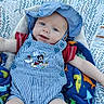 baby, child, blue_hat, striped_overalls, mickey_mouse, blanket, dinosaur_pattern, red_shirt, baby_seat, outdoor, face, smile, infant, cute, young_child, sun_hat, clothing, happy, portrait, person