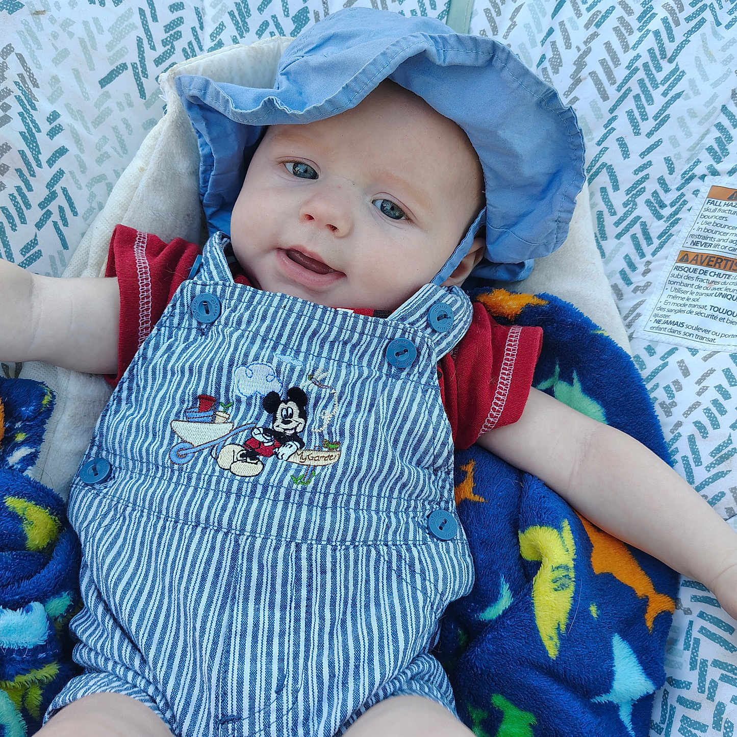 Tyler joined the competition — help win amazing prizes! baby, child, blue_hat, striped_overalls, mickey_mouse, blanket, dinosaur_pattern, red_shirt, baby_seat, outdoor, face, smile, infant, cute, young_child, sun_hat, clothing, happy, portrait, person