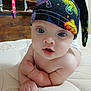 baby, infant, hat, mushroom_pattern, blue_eyes, bare_chest, curious_expression, indoor, mattress, wooden_furniture, child, cute, portrait, skin, person, headwear, colorful, closeup, young, resting