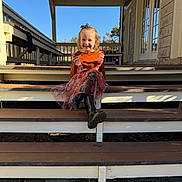 Everleigh is registered to the contest to win money with this photo: child, smiling, girl, orange_clothing, dress, boots, steps, porch, outdoor, daylight, sunny, blue_sky, wood, rustic, autumn, leaves, smile, person, fashion, happy