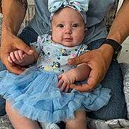 Addaleigh is registered to the contest to win money with this photo: baby, infant, child, blue_dress, headband, adult_hands, tattoo, blanket, patterned_blanket, cute, indoor, portrait, sitting, holding, denim_jeans, watch, skin, expression, person, soft_lighting