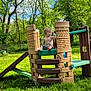 child, toddler, playground, play_structure, plastic, castle, outdoor, grass, trees, sky, sunny, greenery, barefoot, shirtless, nature, summer, daylight, young, curious, person