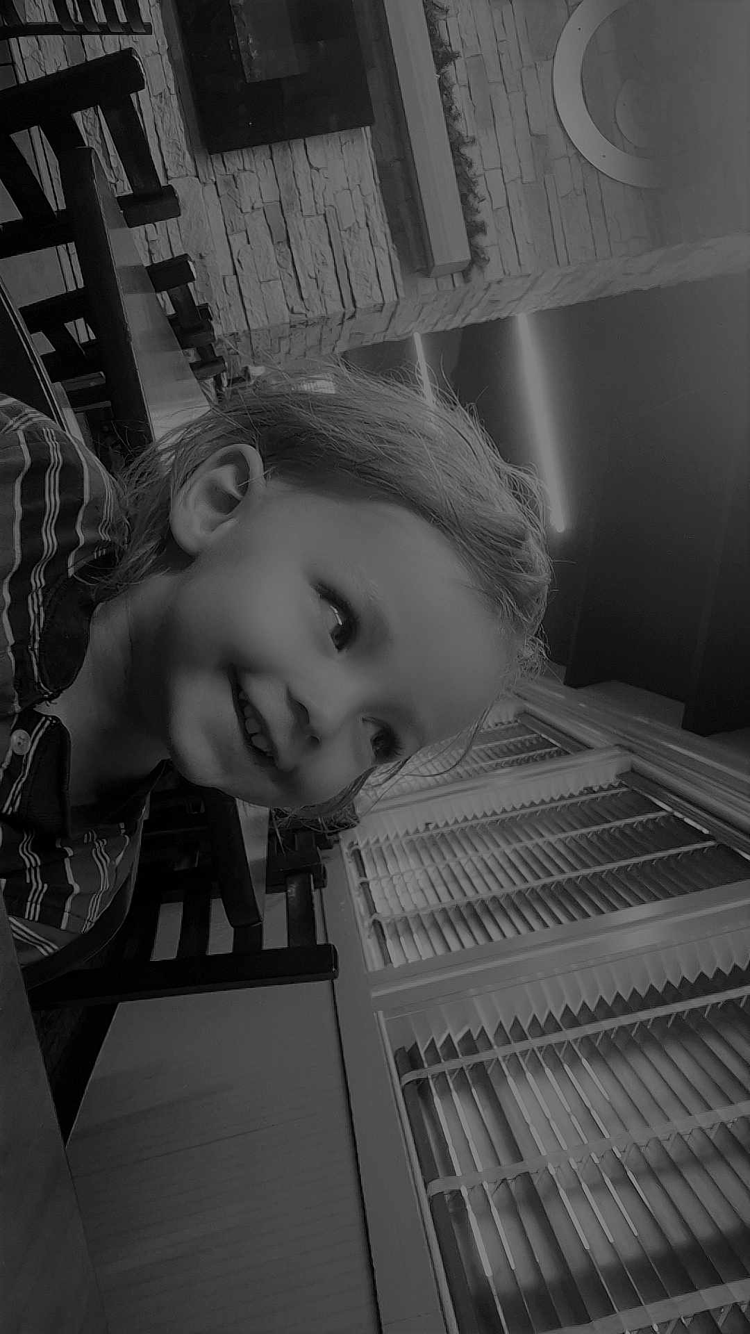 Dennis is registered to the contest to win money with this photo: child, smiling, indoor, window, blinds, wooden_chair, table, hair, face, person, portrait, black_and_white, happy, casual_clothing, light, wall, decor, young, seated, cozy
