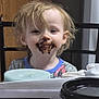 toddler, child, chocolate, messy_face, indoor, table, cup, candle, clothing, hair, face, smile, person, seat, wooden_furniture, background, light, expression, curly_hair, casual