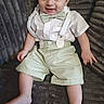 baby, child, smile, suspenders, bow_tie, shorts, shirt, sitting, couch, gray, texture, happy, cute, infant, portrait, indoor, young, person, feet, legs