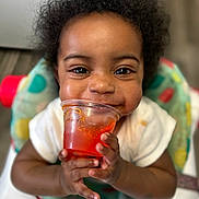 Promise joined the competition — help win amazing prizes! toddler, child, smiling, curly_hair, plastic_cup, orange_drink, high_chair, indoor, happy, face, hands, clothing, food, drink, baby, portrait, cute, closeup, seat, playful