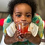 Promise joined the competition — help win amazing prizes! baby, child, face, hands, high_chair, curly_hair, bright_eyes, orange_liquid, plastic_cup, messy_face, indoor, colorful, clothing, smiling, cute, portrait, seat, feeding, close_up, infant