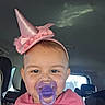 baby, child, pacifier, pink_hat, pink_clothing, car_interior, car_seat, smiling, face, headband, infant, cute, portrait, young_child, seat, vehicle, daylight, happy, closeup, person