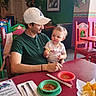 child, toddler, man, restaurant, chips, salsa, table, colorful_chairs, hat, cap, menu, fork, knife, plate, napkin, indoor, food, family, happy, casual