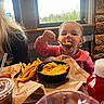 toddler, child, food, macaroni_and_cheese, french_fries, spoon, table, restaurant, window, drink, ketchup, person, pink_clothing, indoor, stone_wall, happy, eating, meal, cute, closeup