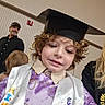child, graduation_cap, sash, curly_hair, smile, indoor, person, adult, man, black_shirt, hat, celebration, event, purple_shirt, happy, family, portrait, people, casual_clothing