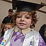 child, graduation_cap, stole, curly_hair, purple_shirt, indoor, family, smile, person, celebration, adult, man, casual_clothing, portrait, background, people, happy, event, sash, closeup