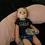 baby, pacifier, bottle, water_bottle, black_shirt, pink_cushion, blue_shorts, infant, child, sitting, indoors, soft_furniture, cute, relaxed, person, young_child, clothing, face, hand, looking_away