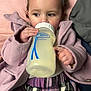 Azura is registered to the contest to win money with this photo: child, toddler, baby_bottle, purple_headband, pink_coat, plaid_skirt, indoor, sitting, drinking, curly_hair, cute, soft_texture, cozy, hand, face, young_child, clothing, person, looking_sideways, relaxed
