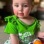 baby, child, toddler, green_clothing, headband, toy, red_toy, indoor, carpet, cute, face, smiling, portrait, sitting, person, curious, closeup, soft_lighting, playful, home