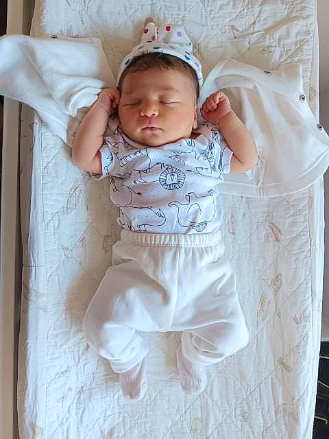Caitlin is registered to the contest to win money with this photo: arm, baby, baby_products, baby_safety, baby_sleeping, baby_toddler_clothing, cap, child, comfort, fashion_accessory, hand, linens, pattern, peach, person, room, sitting, sleeve, t_shirt, textile