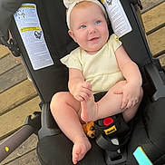 Harper is registered to the contest to win money with this photo: baby, smiling, stroller, headband, blue_eyes, infant, toy, wooden_deck, black_stroller, happy, child, outdoor, foot, clothing, seat, person, cute, summer, playful, baby_girl