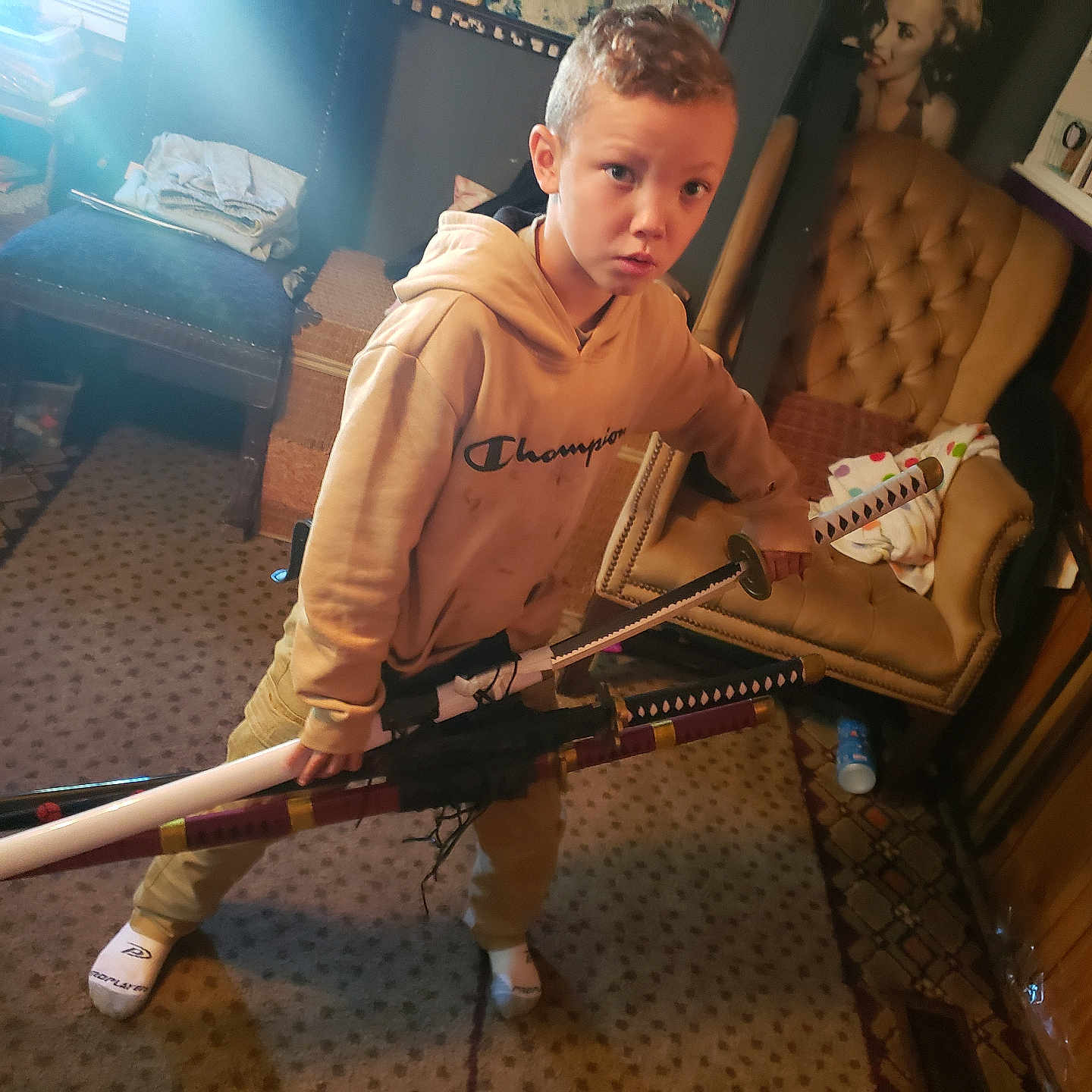 Kamden joined the competition — help win amazing prizes! blanket, carpet, chair, child, expression, floor, furniture, hoodie, indoor, katana, person, portrait, room, shelf, socks, sword, table, toy, weapon, wood_paneling