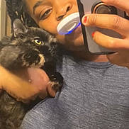 Honey is registered to the contest to win money with this photo: person, cat, selfie, phone, tortoiseshell_cat, indoor, portrait, holding, patterned_curtain, blue_light, smiling, casual_clothing, long_hair, braids, hand, feline, cute, pet, mirror, warm_lighting
