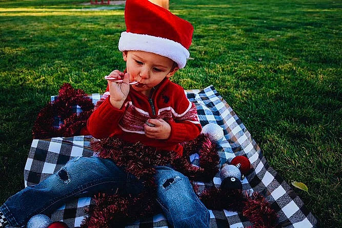 Nolan is registered to the contest to win money with this photo: baby, child, clothing, event, fun, grass, happy, headwear, holiday, lap, leaf, leg, pattern, person, plaid, plant, red, sitting, tartan, textile