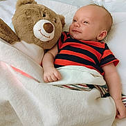 Lucian joined the competition — help win amazing prizes! baby, teddy_bear, blanket, smile, bed, infant, plush_toy, striped_clothing, cute, sleeping_area, comfort, child, soft_toy, happy, resting, indoors, cozy, lying_down, skin, head