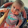baby, child, infant, person, steering_wheel, vehicle_interior, car, shirt, pants, hand, tattoo, floor_mat, seat, window, dashboard, cute, portrait, colorful_clothing, looking_at_camera, holding