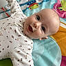 baby, infant, child, playmat, smiling, face, eyes, onesie, clothing, cute, happy, lying_down, colorful, pattern, skin, head, expression, person, indoor, young