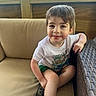 Kyler is registered to the contest to win money with this photo: child, boy, smile, white_tshirt, green_shorts, couch, beige_cushion, wicker_furniture, wooden_wall, outdoor, greenery, portrait, casual, happy, seated, short_hair, daylight, relaxed, cute, young