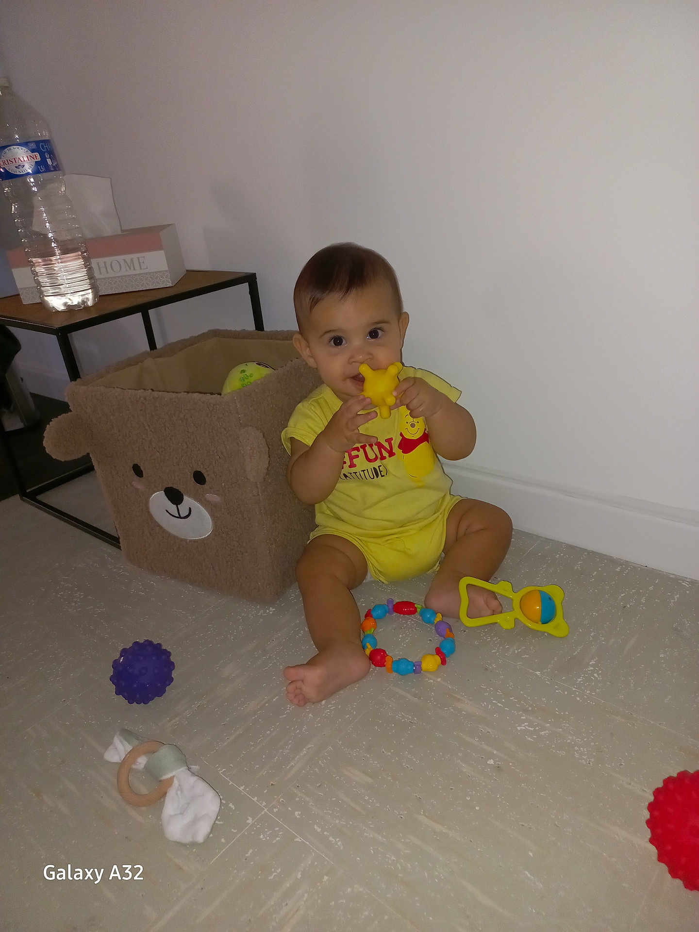 Rafael participe au concours pour gagner de l'argent avec cette photo : baby, bear_design, chewing_toy, child, colorful, curious, cute, expression, floor, home, indoor, plastic_toy, playtime, sitting, storage_basket, table, toddler, toys, water_bottle, yellow_clothing