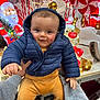 baby, bright, candy_canes, child, christmas_lights, cute, decorations, festive, hands, happy, holding, holiday_display, indoor, person, puffer_jacket, reindeer, santa_claus, smiling, tan_pants, winter_clothing