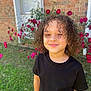 black_tshirt, brick_wall, casual_clothing, child, curly_hair, cute, flower, garden, grass, greenery, happy, nature, outdoor, person, pink_flower, portrait, smile, sunlight, window, young