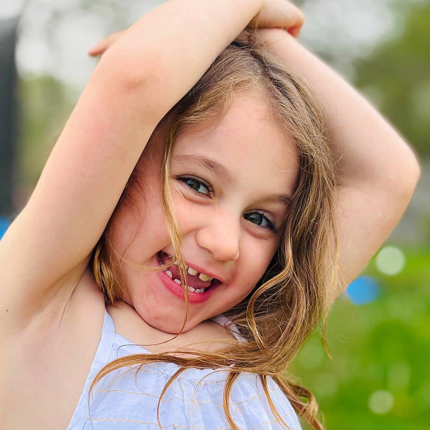 Elyanor is registered to the contest to win money with this photo: arms_up, blond_hair, carefree, casual_clothing, child, closeup, daylight, expression, face, girl, greenery, happy, nature, outdoor, person, playful, portrait, smiling, summer, young