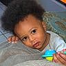 toddler, child, toy, blanket, afro_hair, indoor, television, cartoon, face, hand, earrings, floor, tile, clothing, person, portrait, cute, expression, love, home