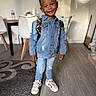 child, boy, denim_jacket, jeans, sneakers, backpack, smile, indoors, wooden_floor, carpet, table, chair, living_room, casual_clothing, person, portrait, happy, standing, young, fashion