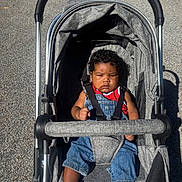 August joined the competition — help win amazing prizes! baby, child, stroller, curly_hair, denim_overalls, red_shirt, white_shoes, outdoor, sunlight, pavement, seatbelt, baby_boy, casual_clothing, infant, cute, young_child, portrait, baby_fashion, transport, daylight