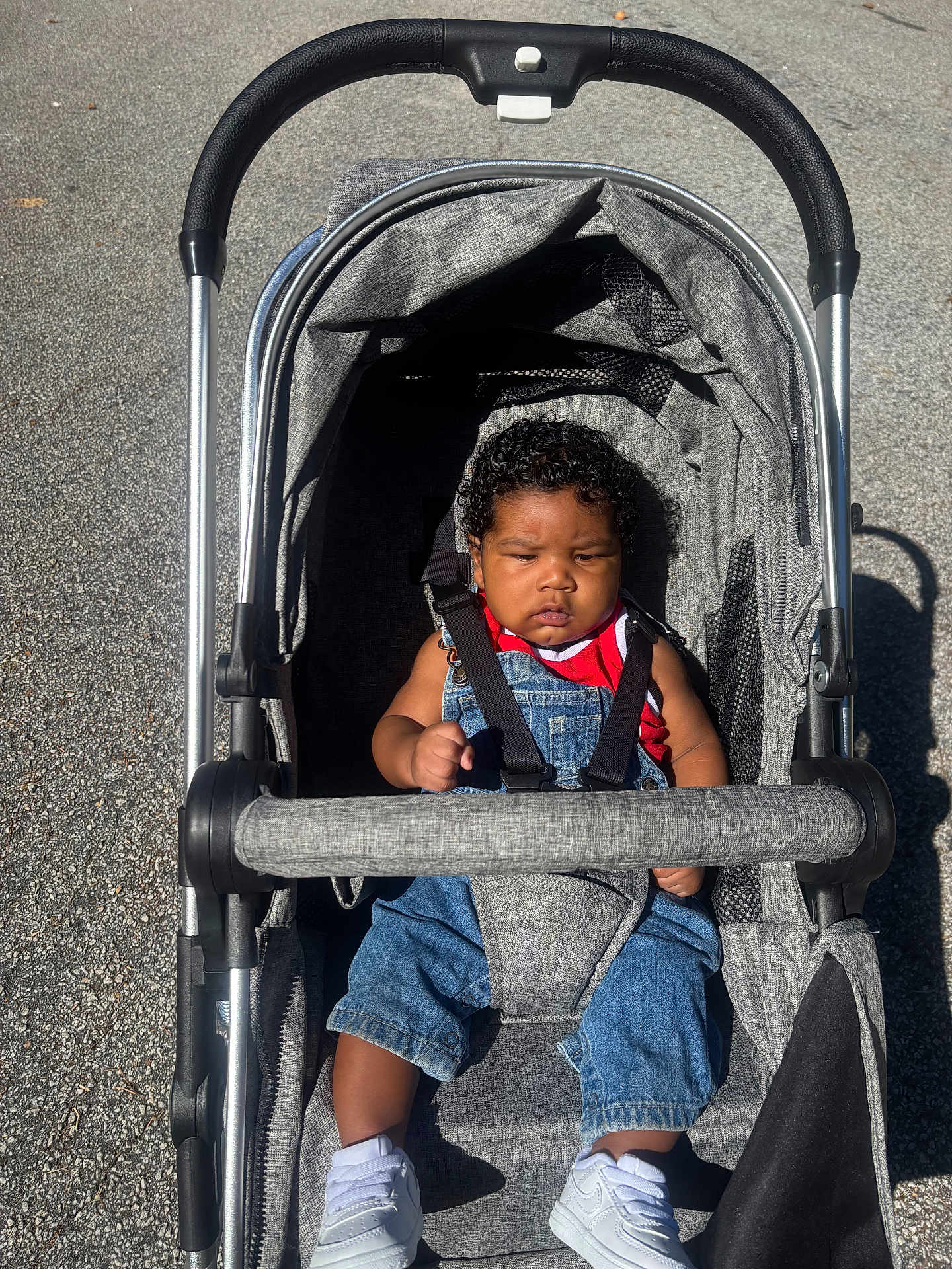 August joined the competition — help win amazing prizes! baby, child, stroller, curly_hair, denim_overalls, red_shirt, white_shoes, outdoor, sunlight, pavement, seatbelt, baby_boy, casual_clothing, infant, cute, young_child, portrait, baby_fashion, transport, daylight