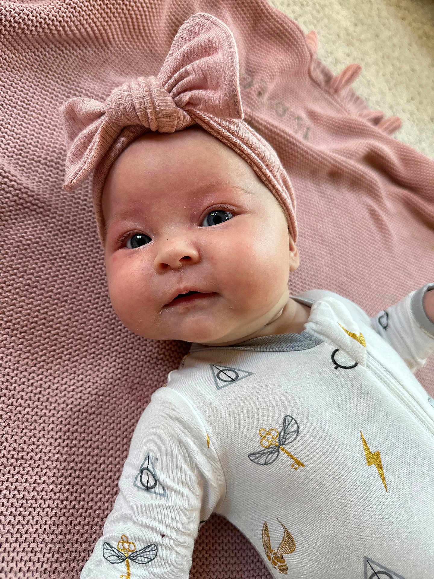 Zoe is registered to the contest to win money with this photo: baby, infant, headband, pink, blanket, onesie, lightning_bolt, key, magic_symbol, face, cute, lying_down, child, soft_texture, closeup, portrait, indoors, apparel, expression, adorable