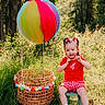 child, girl, toddler, smiling, outdoor, forest, woodland, wildflowers, balloon, rainbow_balloon, basket, chair, red_shirt, checkered_shorts, hair_bows, shoes, sunlight, nature, portrait, playful