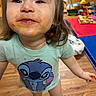 child, curly_hair, cute, floor, happy, home, indoor, messy_face, person, playmat, playtime, portrait, short_sleeves, smiling, socks, stitch_tshirt, toddler, toys, wooden_floor, young_child