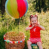 Blakely joined the competition — help win amazing prizes! child, toddler, girl, smiling, outdoor, woodland, forest, meadow, flowers, balloon, rainbow_balloon, wicker_basket, basket, chair, red_shirt, checkered_shorts, hair_bows, sunlight, portrait, nature