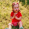 Blakely joined the competition — help win amazing prizes! child, toddler, girl, portrait, outdoor, garden, grass, flowers, daisies, red_shirt, checkered_shorts, hair_bows, smiling, sitting, clasped_hands, shoes, sunlight, nature, colorful, photography