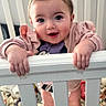 baby, child, crib, pink_bow, smiling, standing, sweater, blanket, indoor, cute, hands, face, person, infant, happy, home, portrait, baby_girl, railing, toy