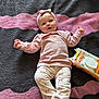 baby, infant, blanket, clothing, headband, face, person, lying_down, diaper_wipes, toy, pink, cream, patterned_pants, soft_texture, indoor, cute, smile, child, happy, cozy