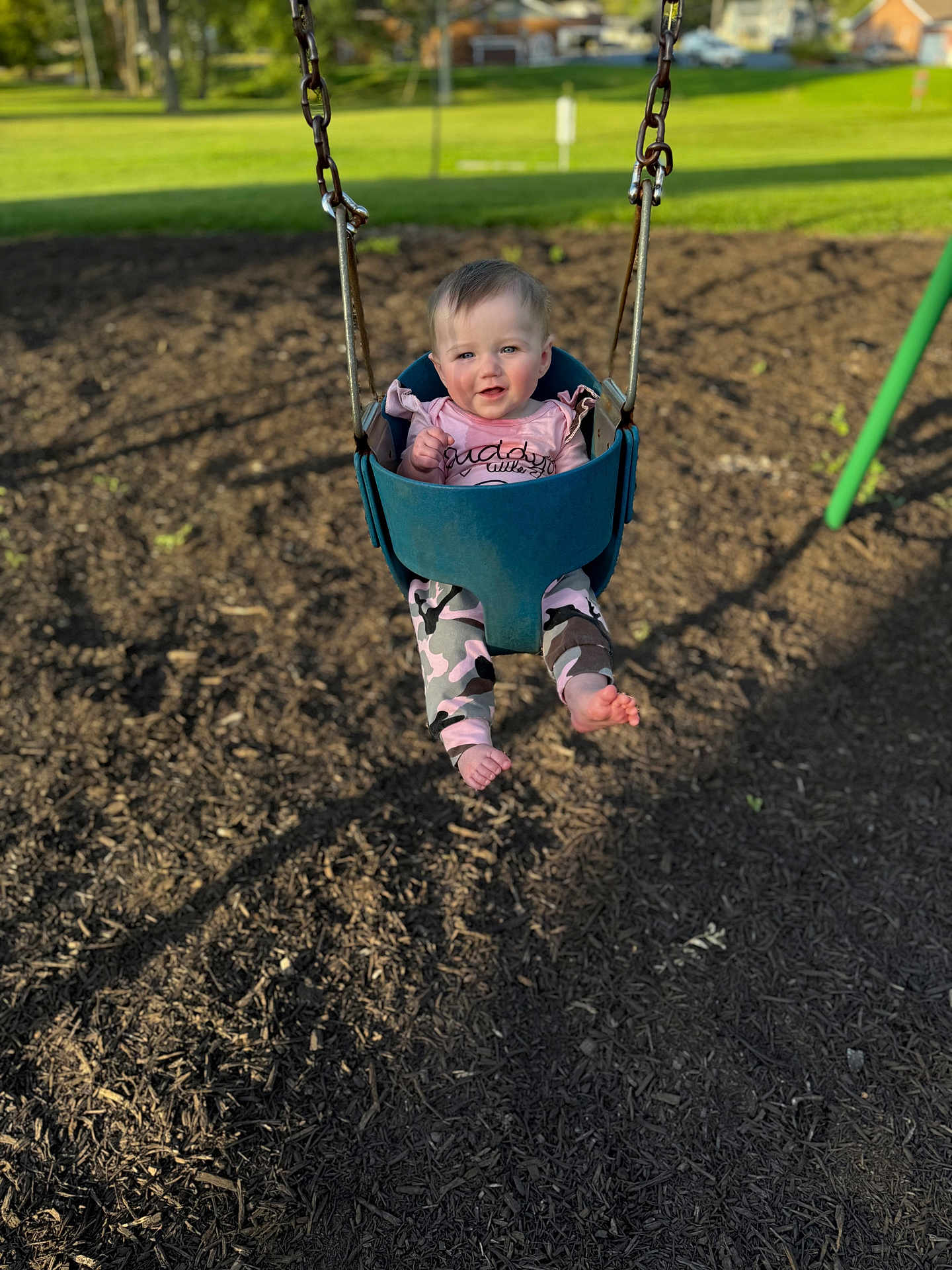Lakelynn is registered to the contest to win money with this photo: baby, child, swing, playground, outdoor, grass, woodchips, sunlight, pink_clothing, camouflage, feet, face, happy, seat, metal_chains, park, young, person, daylight, nature