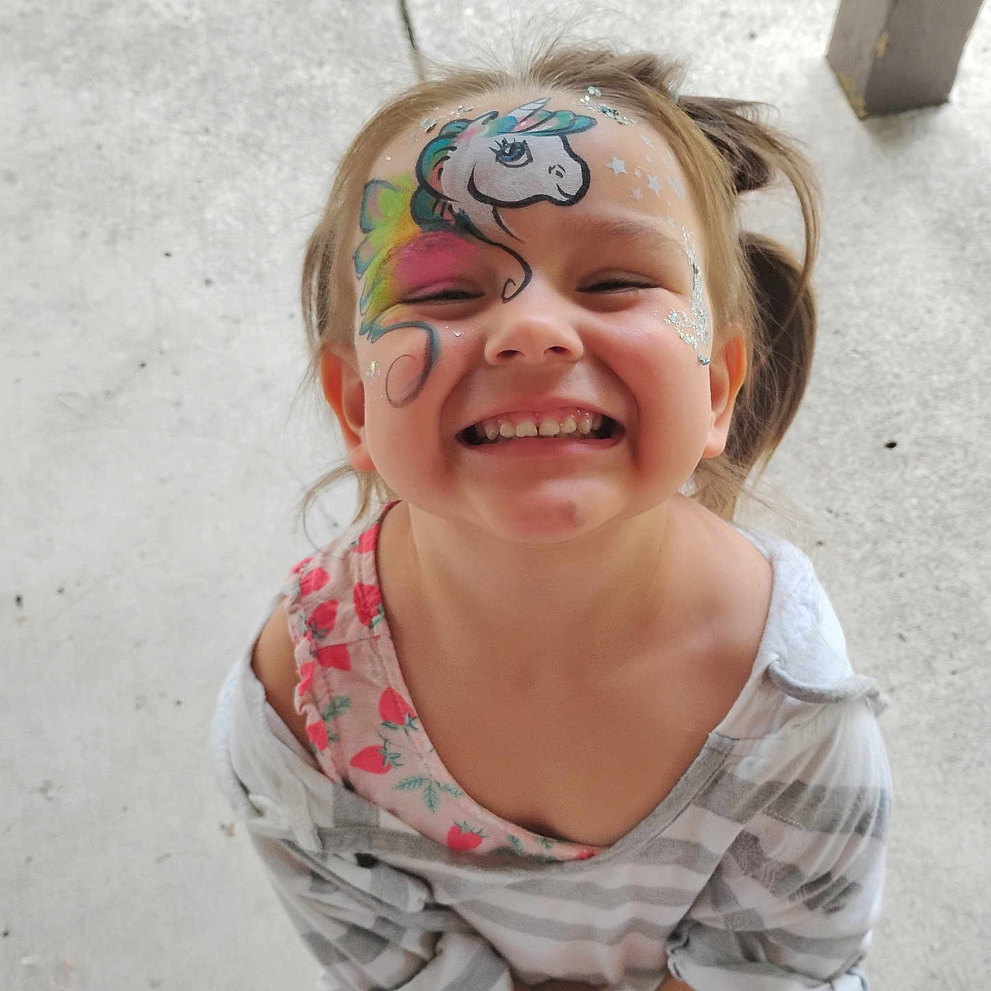 Elizabeth is registered to the contest to win money with this photo: child, face_paint, unicorn, smiling, happy, girl, concrete_floor, striped_shirt, strawberry_pattern, casual_clothing, outdoor, portrait, closeup, playful, young, cute, colorful, sparkles, standing, person