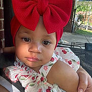 Ketzali is registered to the contest to win money with this photo: toddler, child, red_bow, headband, floral_dress, outdoor, sunlight, brick_wall, garden, person, cute, baby, portrait, face, hand, summer, daylight, holding, expression, casual