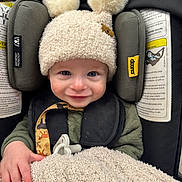 Cooper is registered to the contest to win money with this photo: baby, child, car_seat, hat, pom_poms, blanket, pacifier, smile, face, hand, clothing, green, black, yellow, indoor, infant, cute, comfort, seatbelt, portrait